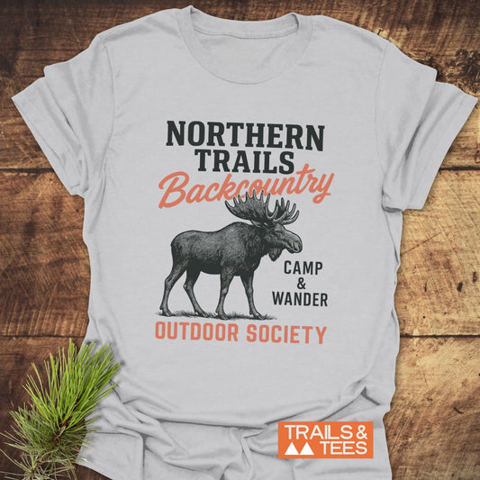 Northern Trails Moose T-Shirt displayed on wood, featuring a moose line-drawing and text. Crafted from soft cotton, durable prints, pre-shrunk for fit, eco-friendly production.