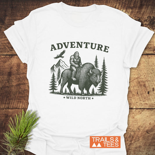 Bigfoot & Bison T-Shirt featuring Sasquatch on a bison with ADVENTURE and WILD NORTH text. Soft, durable cotton by Trails & Tees.