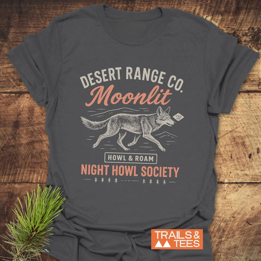 Night Howl Society T-Shirt featuring a stylized coyote print on charcoal-gray, made from soft ring-spun cotton. Laid on wood with an orange Trails & Tees logo.