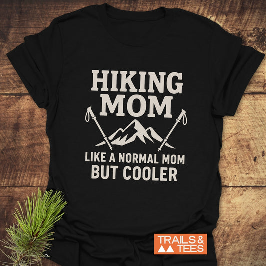 Black T-shirt with Hiking Mom mountain graphic and hiking poles, showcasing Trails & Tees logo. Crafted for comfort, ideal for outdoor enthusiasts.