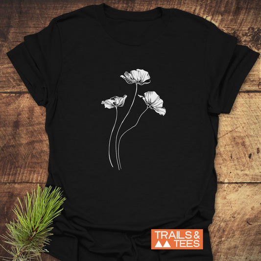 Delicate Poppies T-Shirt featuring white poppy line-drawing on black, emphasizing comfort and adventure-ready design, with TRAILS & TEES logo visible.