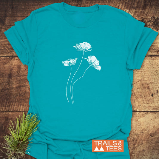 Delicate Poppies T-Shirt with white poppy line drawing on front, laid flat with pine sprig. Features soft ring-spun cotton, durable print, pre-shrunk.