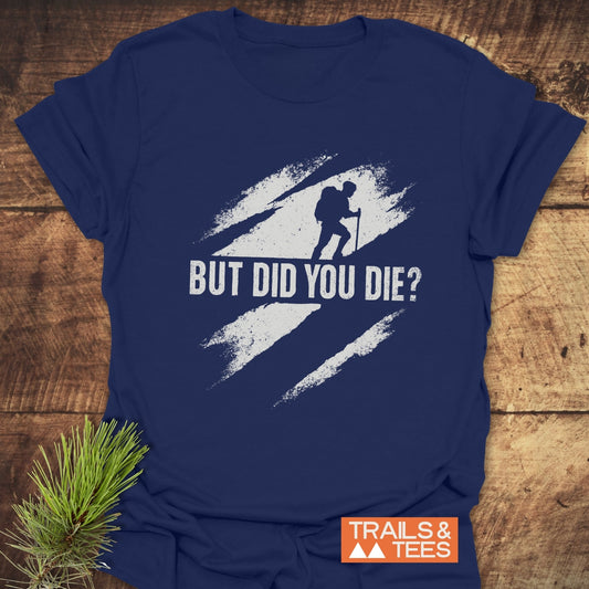 But Did You Die? Hiking T-Shirt featuring a distressed white backpacker graphic with bold text, laid on wood with pine sprig, next to TRAILS & TEES logo.