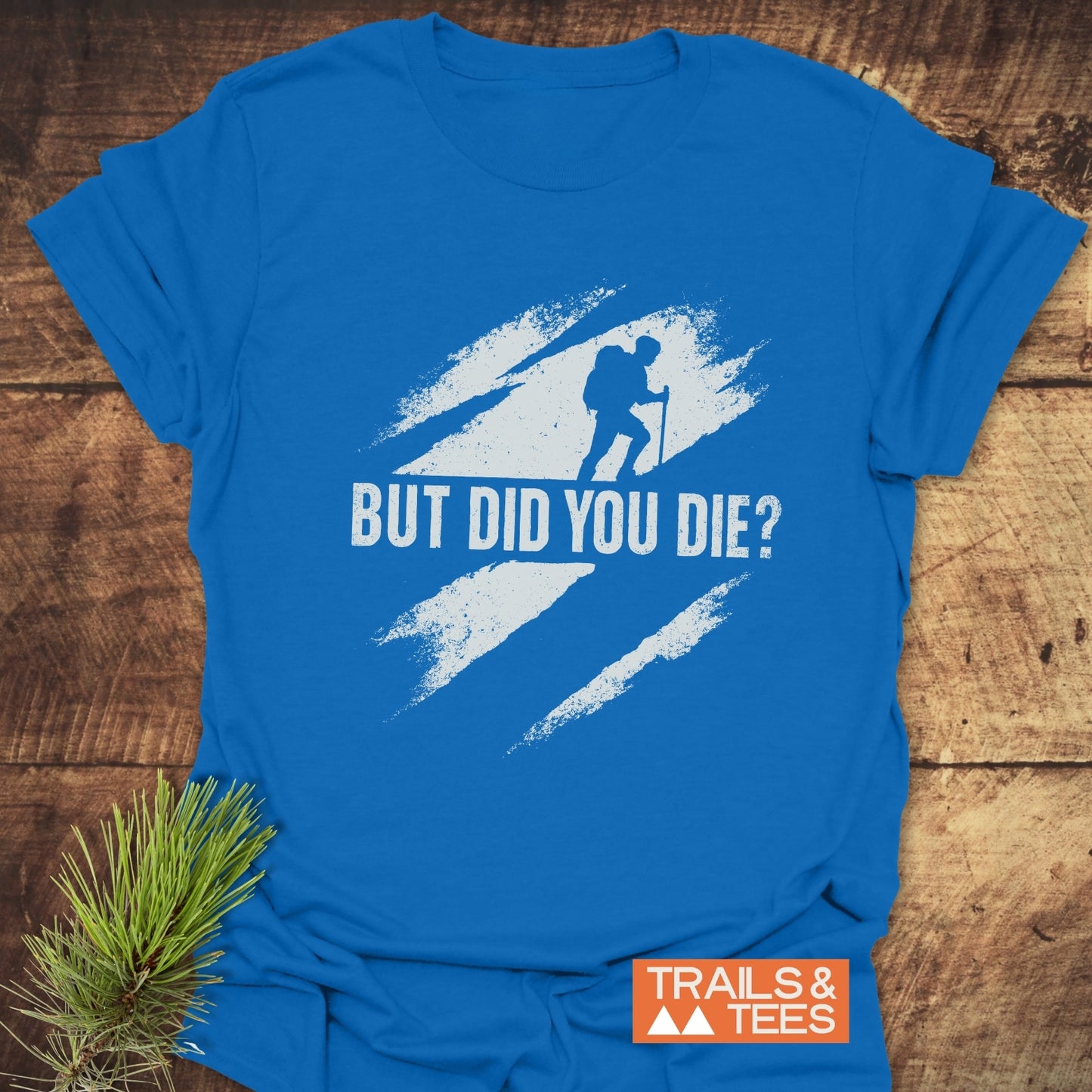But Did You Die? Hiking T-Shirt featuring a hiker silhouette and slogan, crafted from soft cotton for comfort and durability, displayed on a wooden surface.