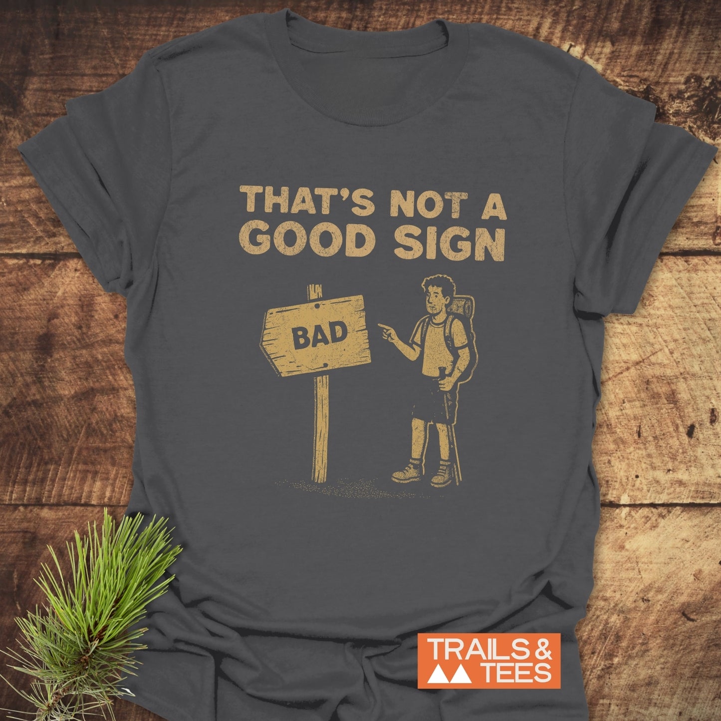 Bad Sign Funny T-Shirt: Charcoal-gray tee with a distressed yellow-tan print showing a hiker pointing at a crooked sign. Soft, lightweight, ring-spun cotton.