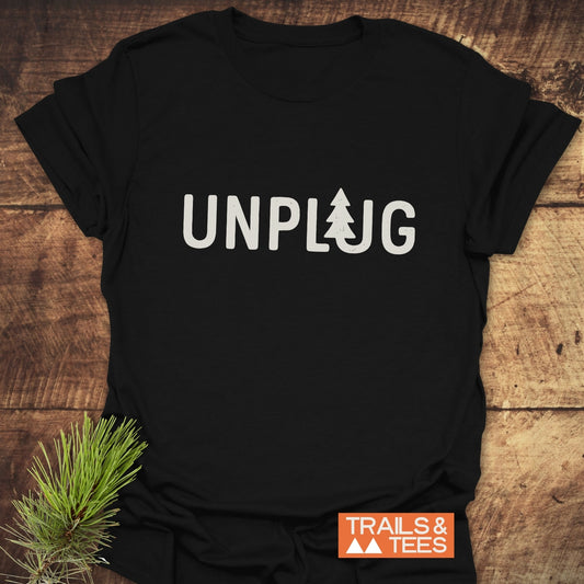Unplug T-Shirt with pine tree icon on front, laid beside a pine branch; features durable print, pre-shrunk fit, and nature-inspired design.