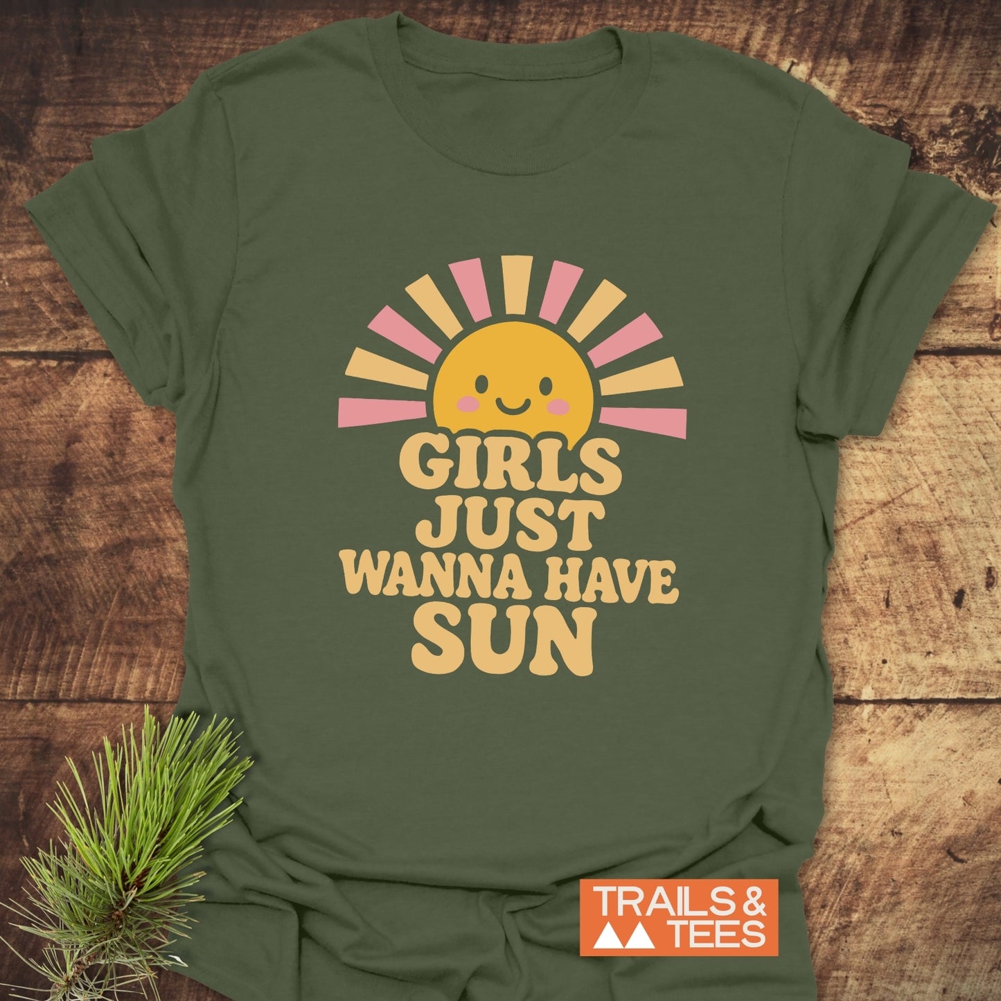 Green Girls Want Fun T-Shirt with retro-style smiling sun print, laid on wood. Features soft cotton, pre-shrunk fit, durable print, Trails & Tees logo.