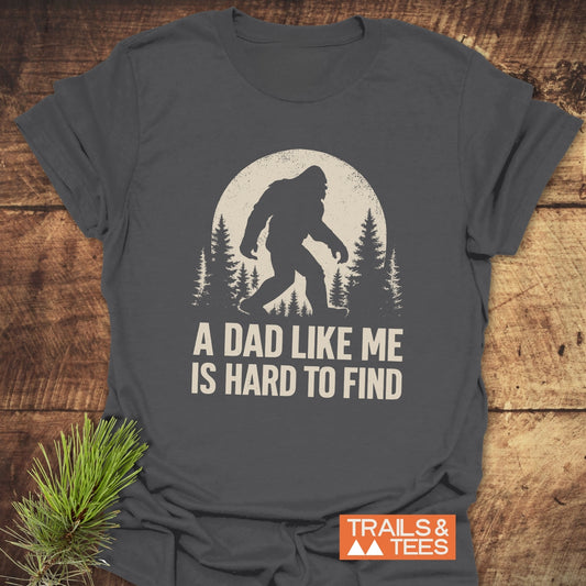 Vintage Bigfoot Dad T-Shirt with Sasquatch graphic and A DAD LIKE ME IS HARD TO FIND text, laid on wood, featuring durable, soft ring-spun cotton.