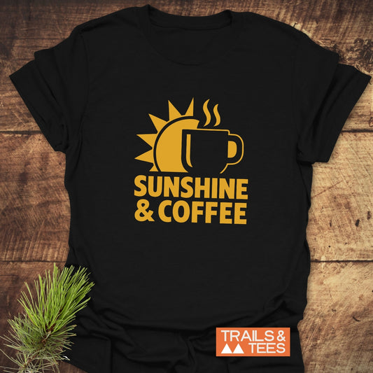 Bold Sunshine & Coffee T-Shirt on wood, featuring a gold sun and coffee mug design. Includes “TRAILS & TEES” logo, highlighting adventure-ready comfort and durable prints.