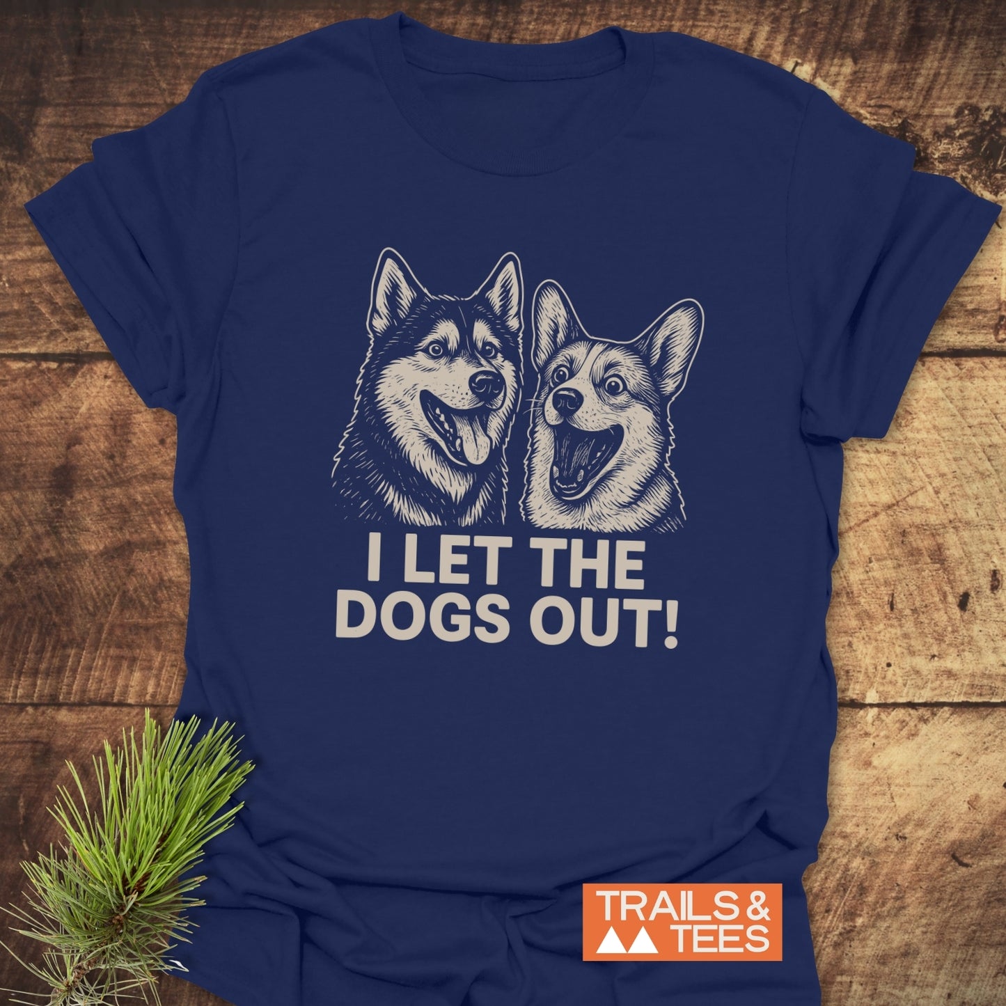 Navy I Let The Dogs Out T-shirt with cartoon husky and corgi, lightweight cotton, logo TRAILS & TEES, laid on wood with pine sprig.