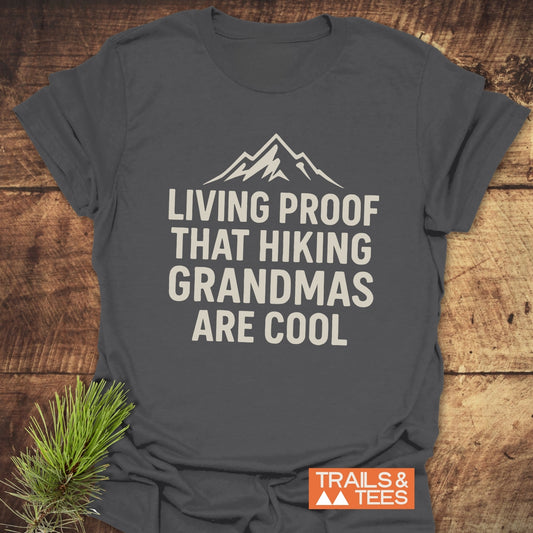 Living Proof Grandma T-Shirt with mountain graphic and slogan, laid on wood. Made from soft, lightweight cotton, perfect for outdoor enthusiasts. TRAILS & TEES logo visible.