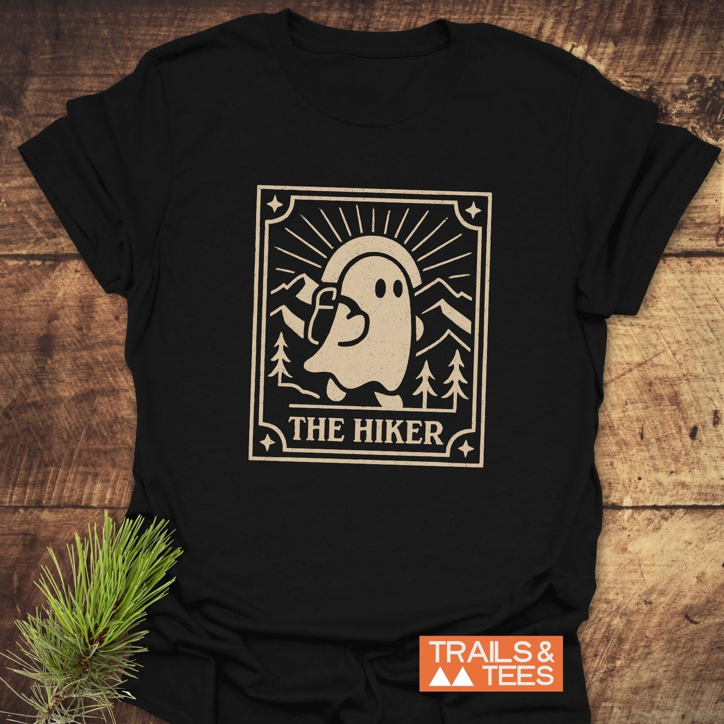 The Hiker Retro Tarot T-Shirt showcases a ghost hiker illustration with pine trees and mountains, offering soft, durable comfort ideal for outdoor enthusiasts.