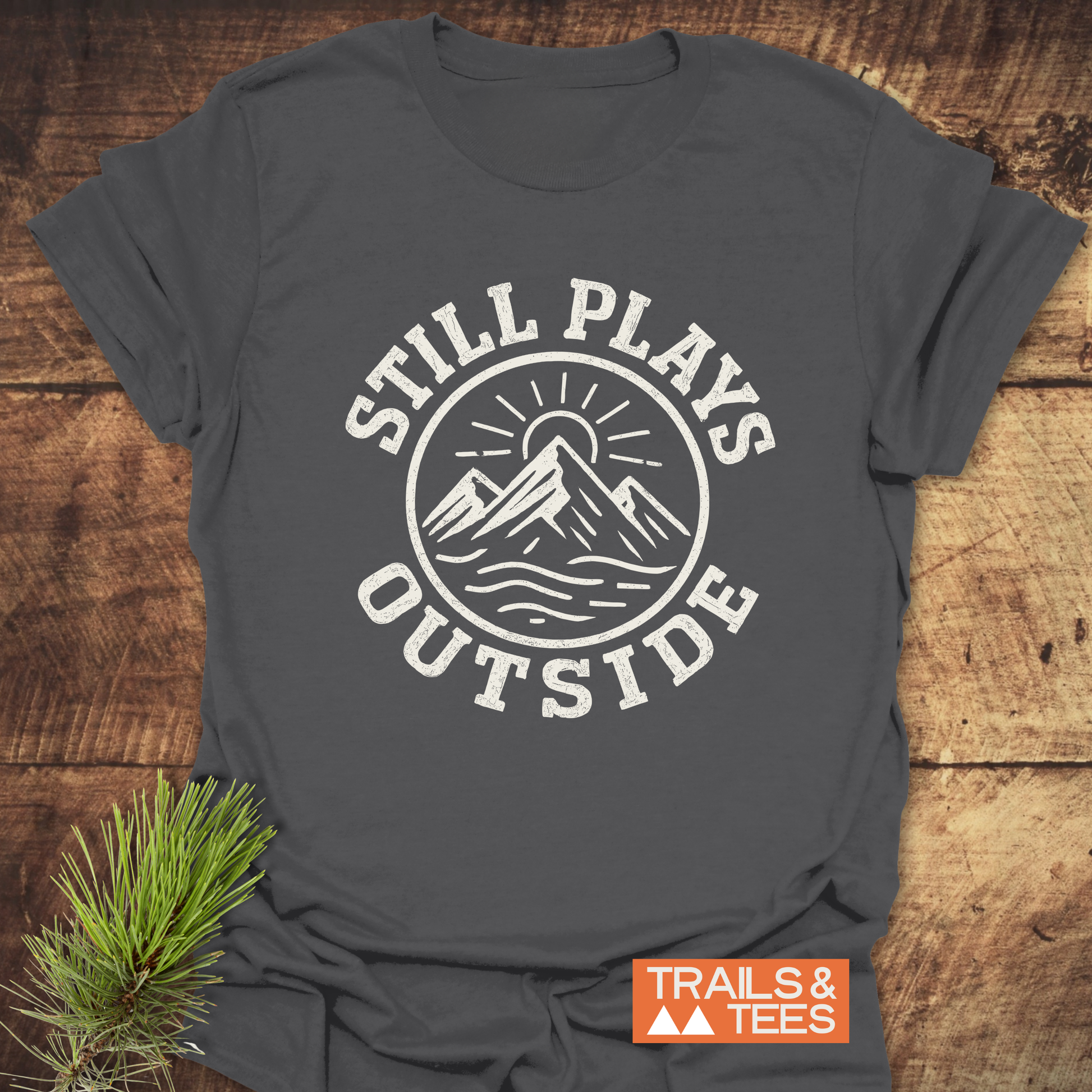 The Still Plays Outside T-Shirt features a distressed mountain graphic, showcasing outdoor spirit, on soft ring-spun cotton, ideal for adventure enthusiasts.