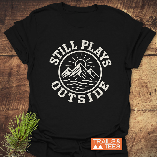 Still Plays Outside T-Shirt featuring a distressed mountain and sun graphic, showcasing outdoor spirit. Made from soft ring-spun cotton for comfort and durability.