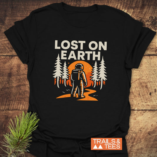 Lost On Earth T-Shirt featuring an astronaut graphic amidst pine trees and an orange sun, highlighting outdoor adventures, crafted from soft, lightweight cotton for comfort.
