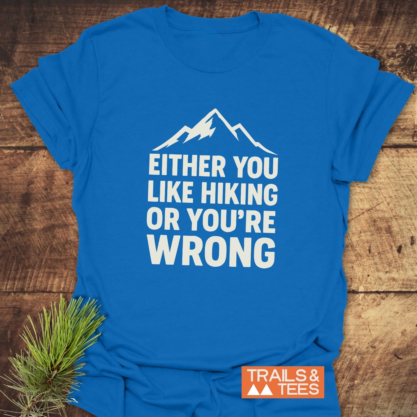 Either You Like Hiking T-Shirt with white mountain graphic and bold slogan, laid on wood with pine sprig; crafted from soft, durable cotton.