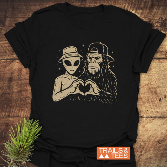 Strange Love Bigfoot T-Shirt featuring an alien and Bigfoot forming a heart with their hands, showcasing durable print on soft, pre-shrunk cotton.