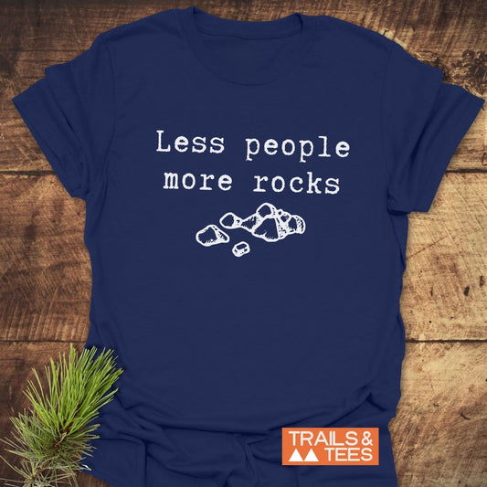 Navy-blue Less People More Rocks T-shirt with typewriter-style slogan and rock illustration, laid on rustic surface. Features durable, soft ring-spun cotton for outdoor enthusiasts.