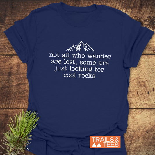 Looking For Cool Rocks T-Shirt features a white mountain graphic and phrase on navy-blue cotton, emphasizing comfort and adventure, with Trails & Tees logo.