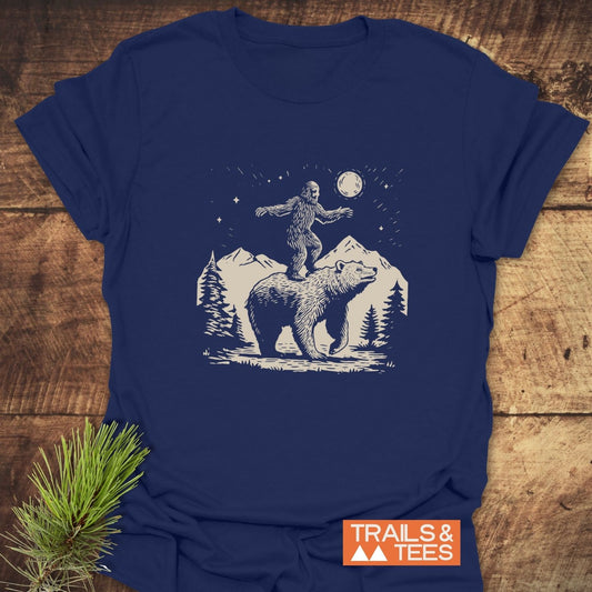 Bigfoot And Bear Funny T-Shirt featuring a bear in mountain scene with sasquatch. Trail-tested comfort, lightweight cotton, pre-shrunk, and durable print.