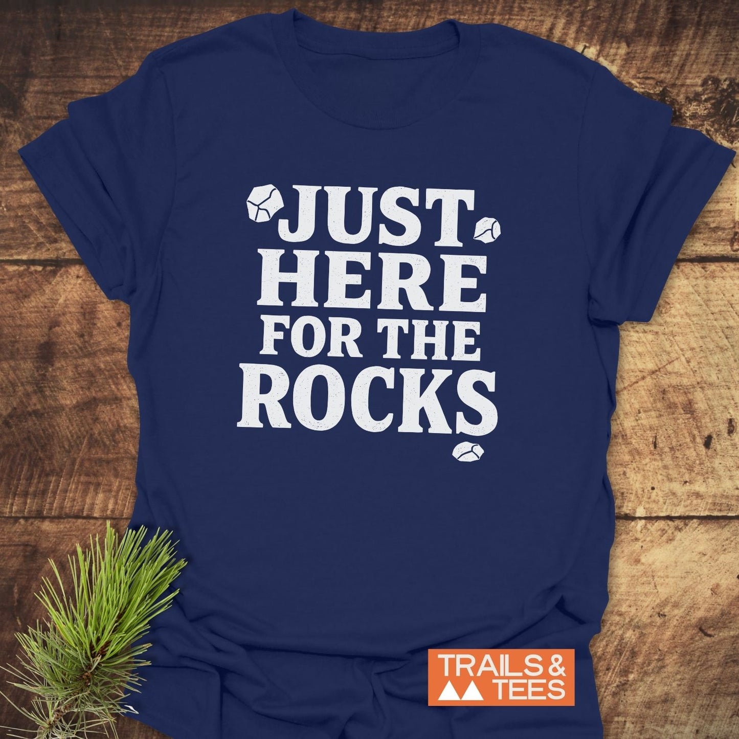 Navy T-shirt reading JUST HERE FOR THE ROCKS with rock illustrations, featuring the TRAILS & TEES logo, emphasizes outdoor adventures and comfort.