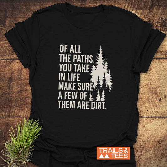 Black Of All The Paths T-shirt with white pine tree graphic and slogan, laid flat on wood. Features include ring-spun cotton, durable print, and taped shoulders.