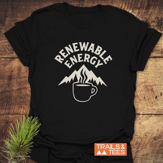 Renewable Energy T-Shirt featuring mountain and coffee mug graphic, laid on wood with pine sprig, designed for comfort and sustainability.