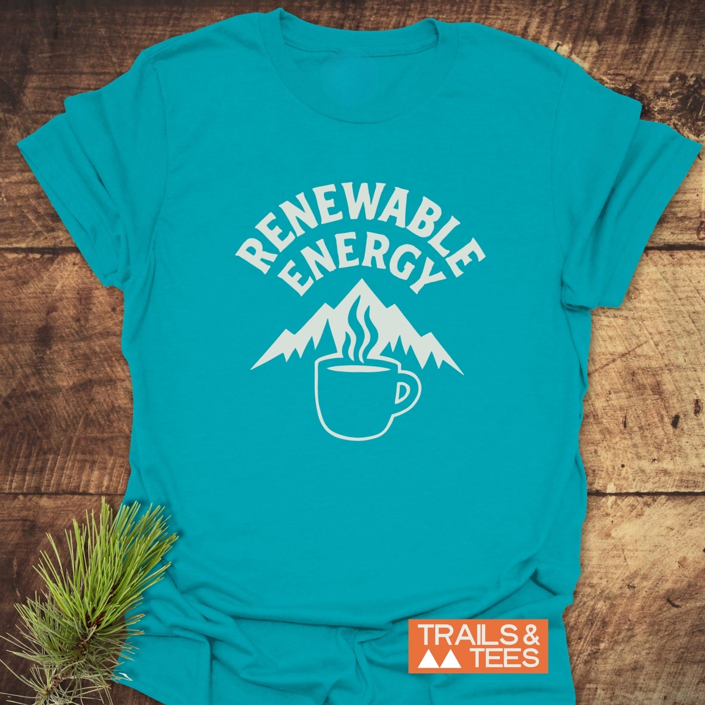 Renewable Energy T-Shirt featuring mountain peaks in a coffee mug graphic, crafted from soft cotton with durable prints, laid on a wooden surface.