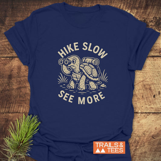 Navy-blue Hike Slow Funny T-Shirt with a hiking tortoise design, slogan, and Trails & Tees logo, crafted from soft, durable cotton for outdoor enthusiasts.