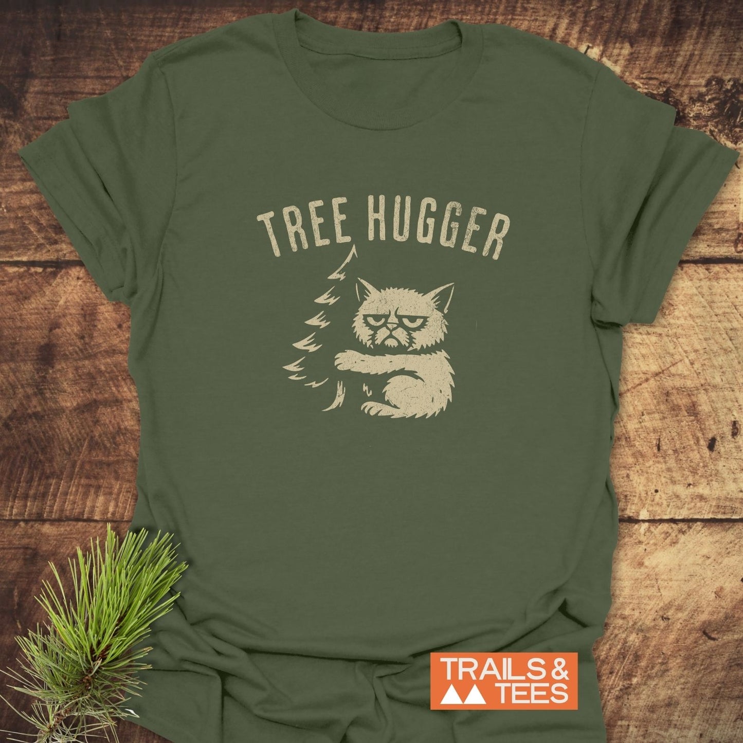 Tree Hugger Funny T-Shirt with a grumpy cat hugging an evergreen tree graphic, made from soft, lightweight cotton for everyday outdoor adventures.