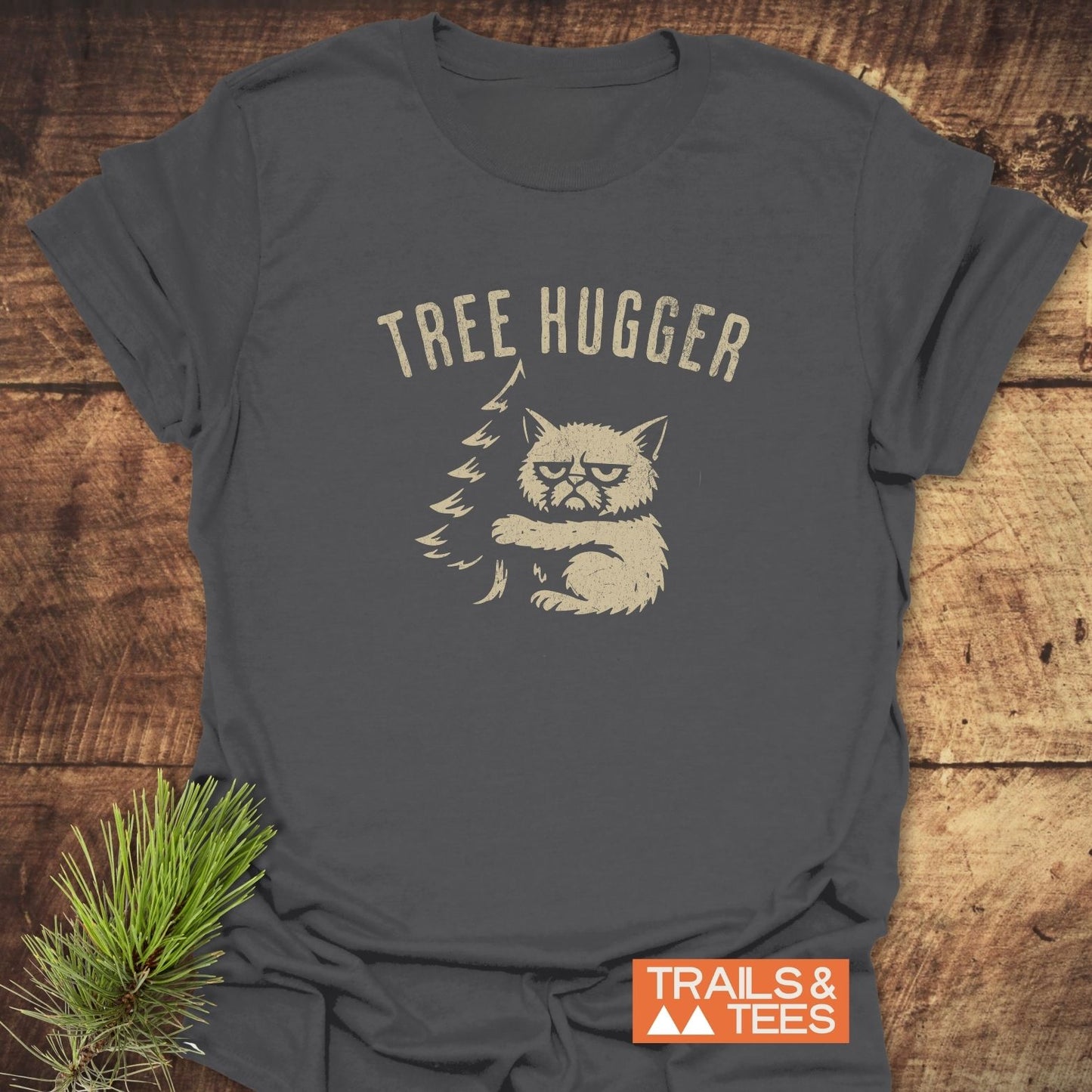 Tree Hugger Funny T-Shirt featuring a scowling cat hugging a pine tree, printed on soft, lightweight cotton, ideal for outdoor enthusiasts.