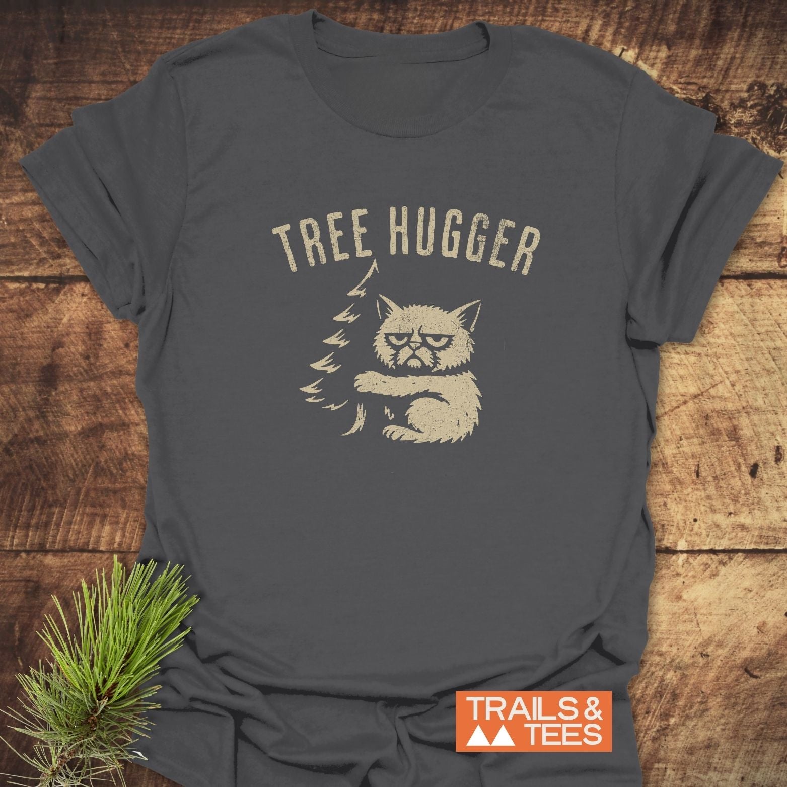 Tree Hugger Funny T-Shirt featuring a scowling cat hugging a pine tree, printed on soft, lightweight cotton, ideal for outdoor enthusiasts.