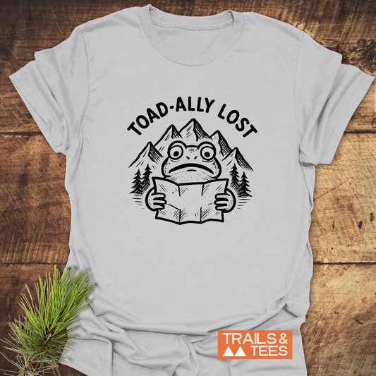 Toad-ally Lost T-Shirt featuring a cartoon frog with a map amidst pine trees and mountains, highlighting outdoor adventure; crafted for comfort and durability.
