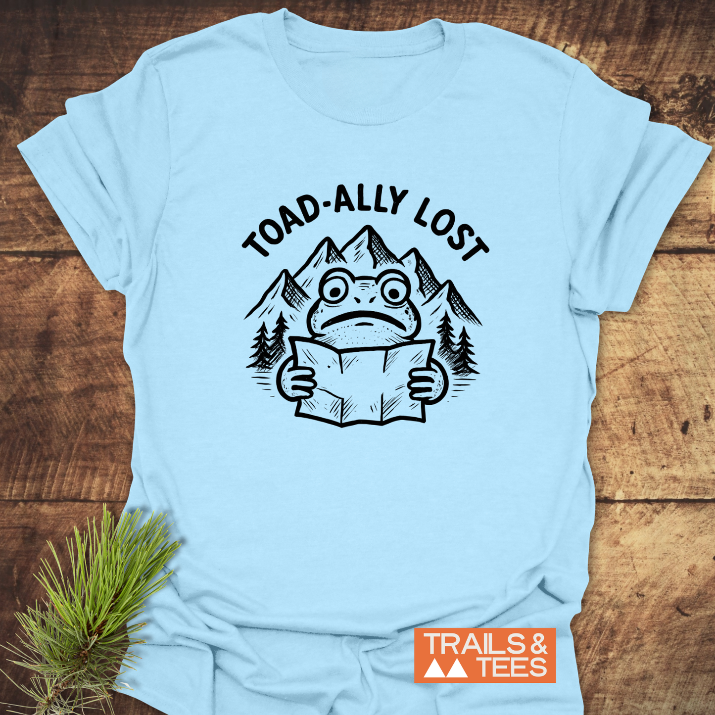 Toad-ally Lost T-Shirt featuring a cartoon toad with a map, set against mountains. Made from soft cotton with durable prints, perfect for outdoor adventures.
