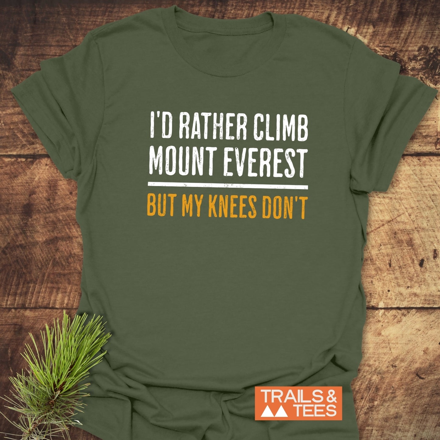 I'd Rather Climb Mt Everest T-Shirt on wood surface, featuring distressed lettering, with 'TRAILS & TEES' logo. Soft, ring-spun cotton for outdoor enthusiasts.