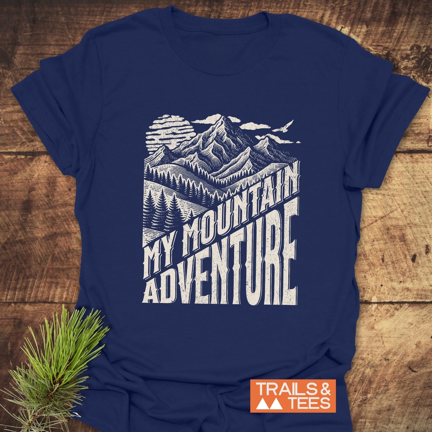 My Mountain Adventure T-Shirt with a stylized mountain scene and bold text, crafted from soft cotton for comfort, featuring durable prints and a small Trails & Tees logo.