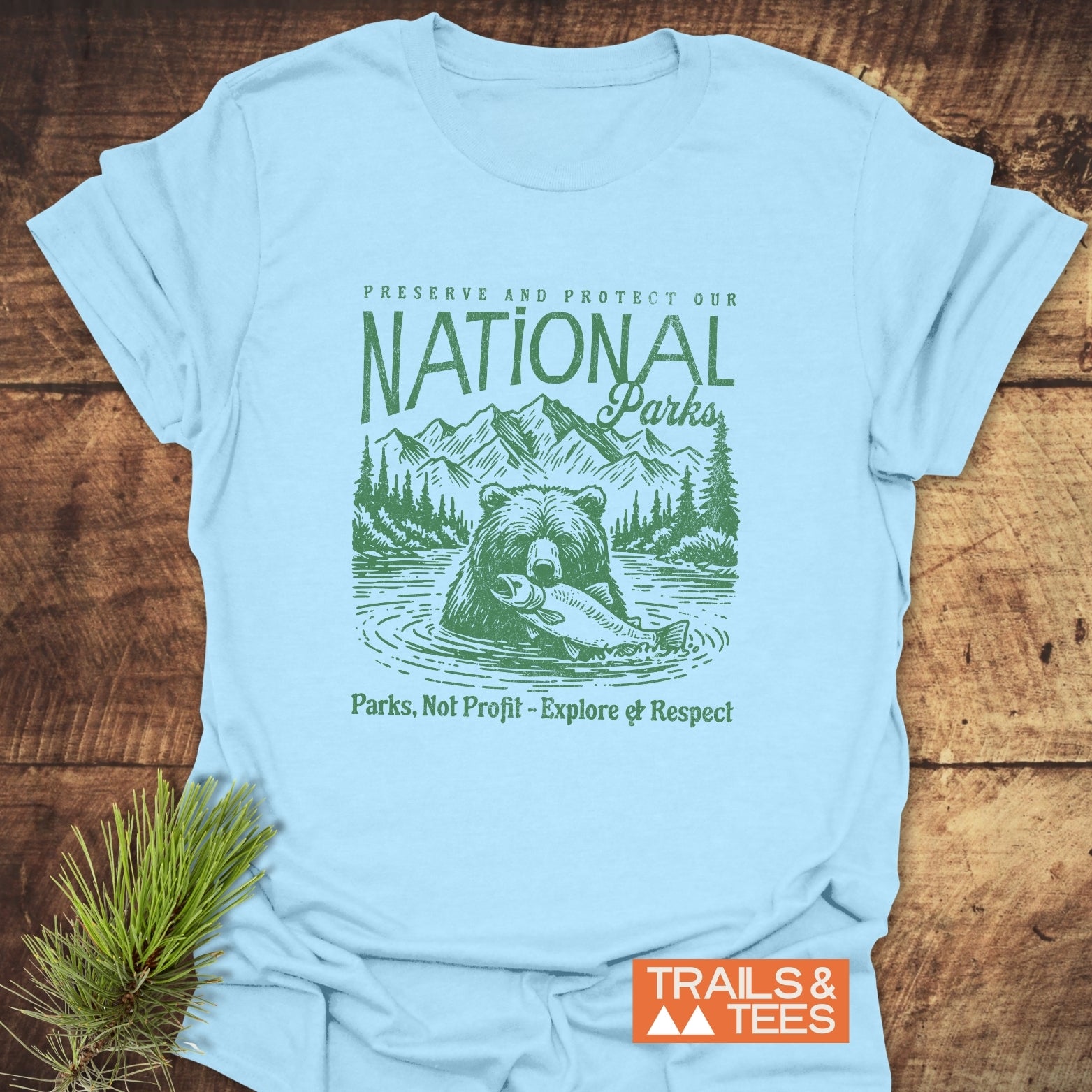 National Parks T-Shirt featuring a bear with a fish, set against mountains. Slogan emphasizes park conservation. Crafted from soft, durable cotton for outdoor adventures.