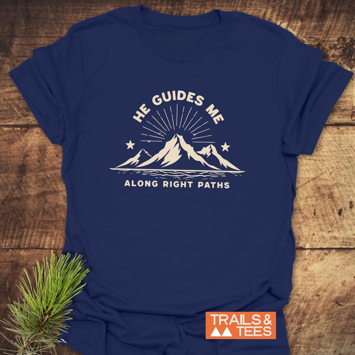 Navy-blue He Guides Me T-shirt with mountain design, sunrays, stars, and river. Features durable print, soft cotton, and TRAILS & TEES label.
