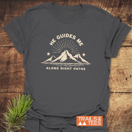 He Guides Me T-Shirt with mountain design and sunbeams, crafted from soft cotton for comfort and durability, featuring the Trails & Tees logo on the corner.