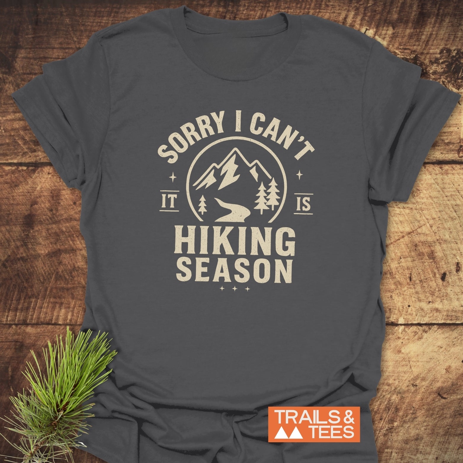 Charcoal-gray 620 Hiking Season T-Shirt featuring a mountain graphic and hiking season slogan, emphasizing comfort and adventure. Includes small orange TRAILS & TEES logo.