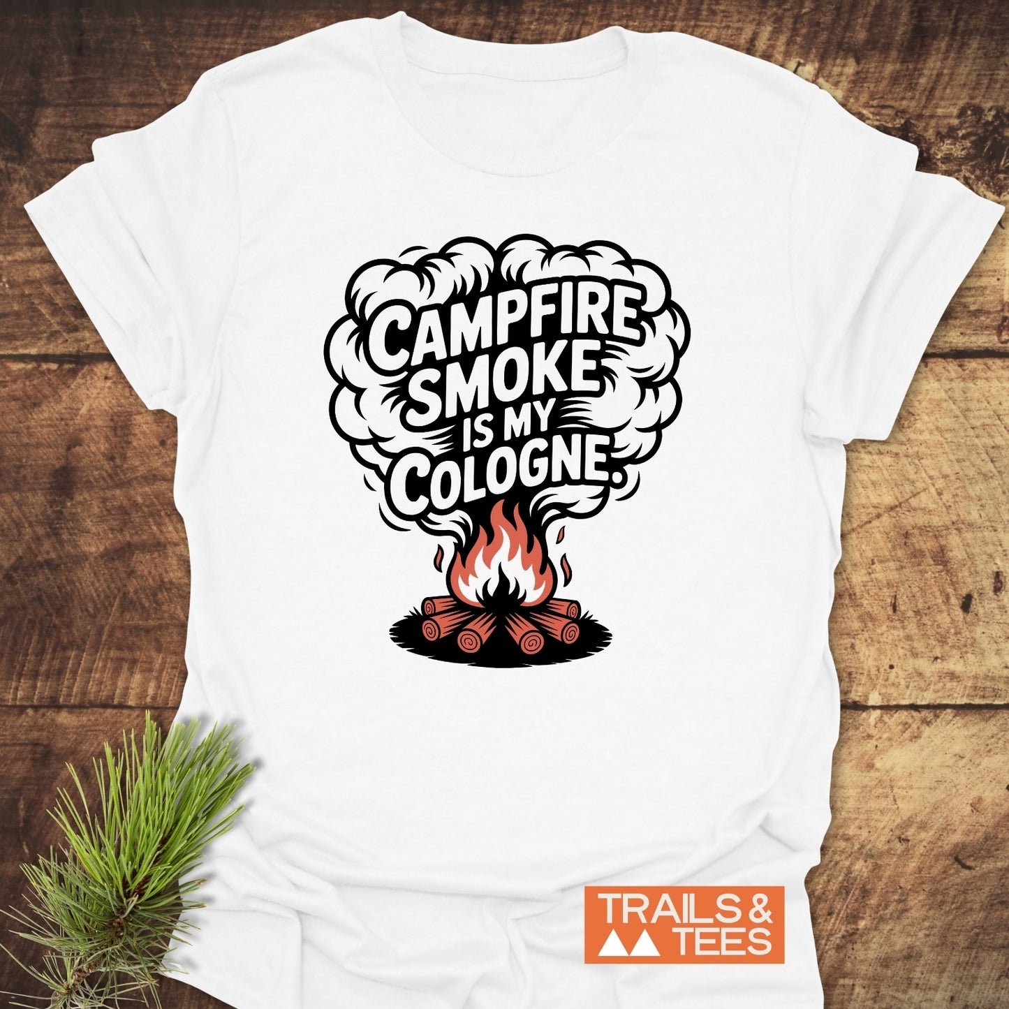 Campfire Smoke Funny T-Shirt with a stylized campfire print, laid on wood. Features durable print, pre-shrunk cotton, and Trails & Tees logo.