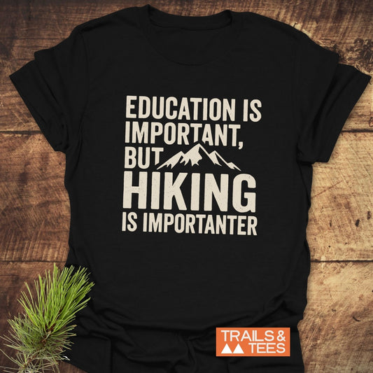 Black T-shirt with Education Is Important, But Hiking Is Importanter slogan, mountain graphic, and TRAILS & TEES logo, highlighting outdoor adventure and comfort.