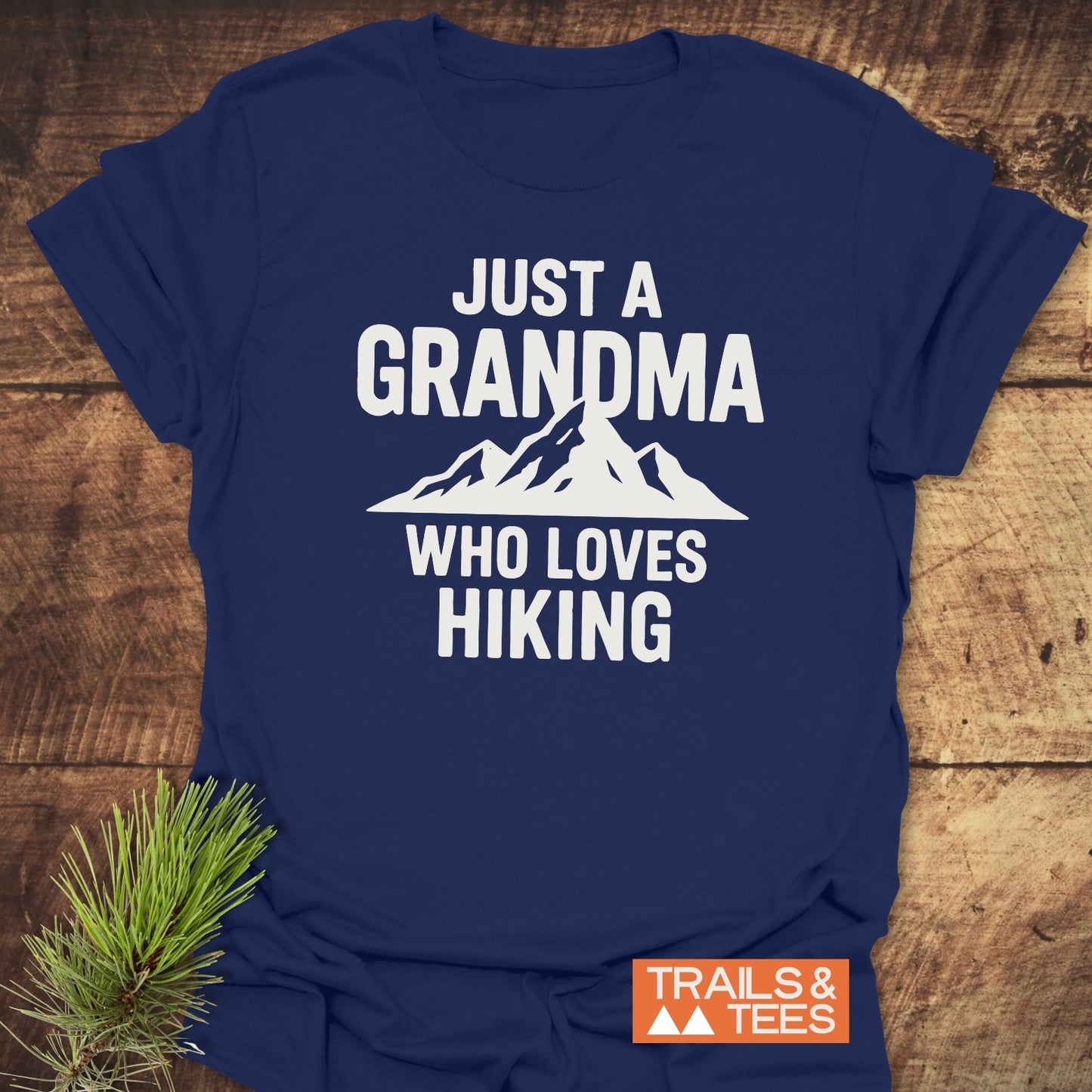 Navy-blue Grandma Loves Hiking T-Shirt with mountain graphic. Features soft ring-spun cotton, durable print, and taped shoulders for comfort. Trails & Tees logo visible.