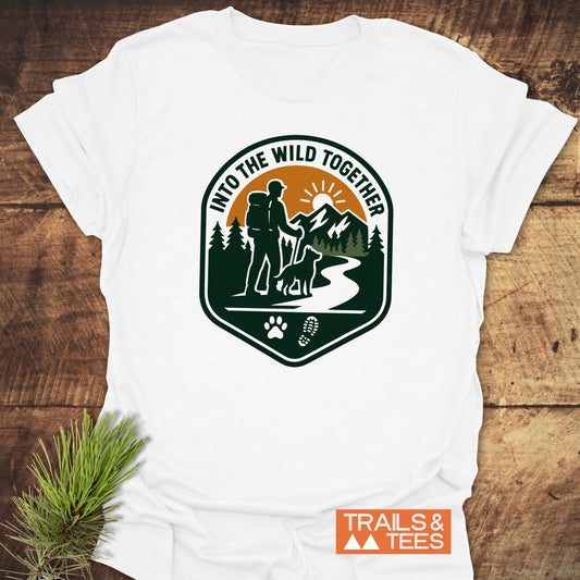 Into The Wild T-Shirt featuring a hiking graphic with a backpacker, dog, and nature scenery, highlighting comfort and adventure, designed for outdoor enthusiasts.