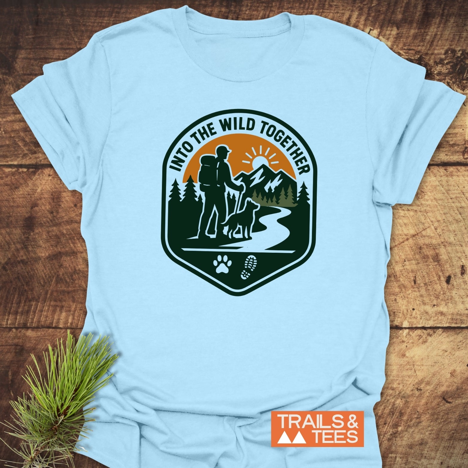 Into The Wild T-Shirt featuring a backpacker and dog graphic with INTO THE WILD TOGETHER, paw print, boot track icons, and TRAILS & TEES branding.