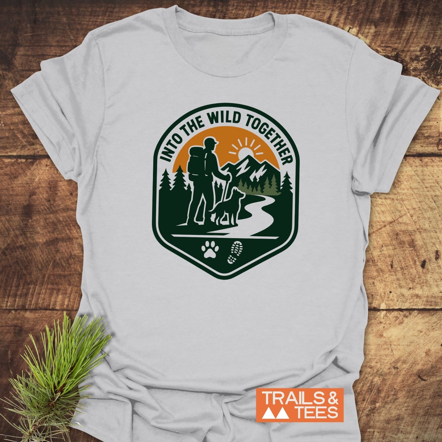 Into The Wild T-Shirt features a hiking-themed badge graphic, emphasizing outdoor adventure, crafted from soft cotton for comfort and durability, with sustainable, fast-shipping production.