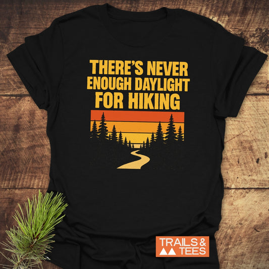 Never Enough T-Shirt with sunset graphic and evergreen silhouette, featuring “THERE’S NEVER ENOUGH DAYLIGHT FOR HIKING,” highlighting durable, adventure-ready comfort by Trails & Tees.