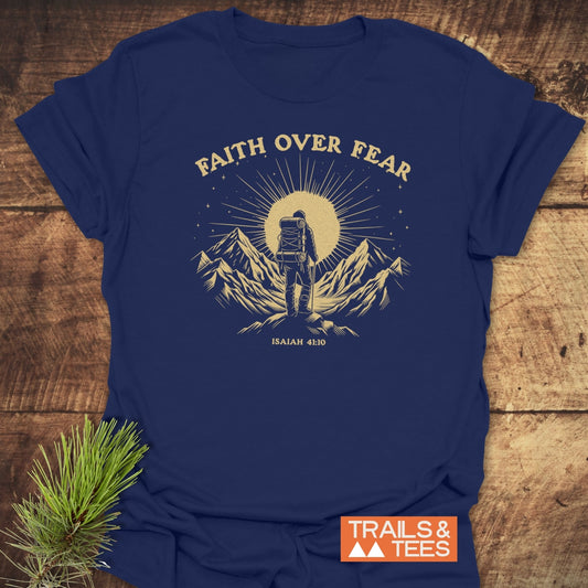 Faith Over Fear T-Shirt with vintage backpacker graphic, radiating sunburst, stars, slogan, and Isaiah 41:10 reference, laid on a rustic surface.