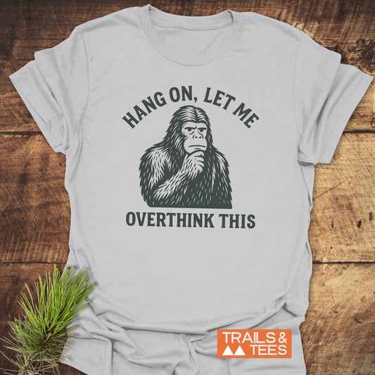 Bigfoot Overthinking T-Shirt featuring a thoughtful ape-like creature and the text “HANG ON, LET ME OVERTHINK THIS,” designed for comfort and outdoor adventures.