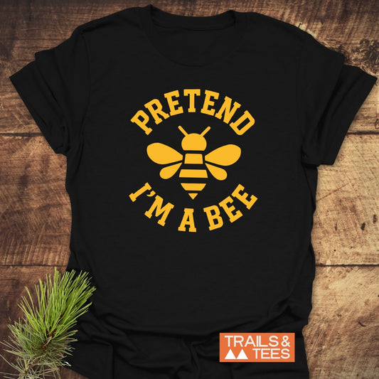 I'm A Bee Funny T-Shirt featuring a yellow bee graphic and collegiate text on soft black cotton, styled with an evergreen sprig for outdoor vibes.